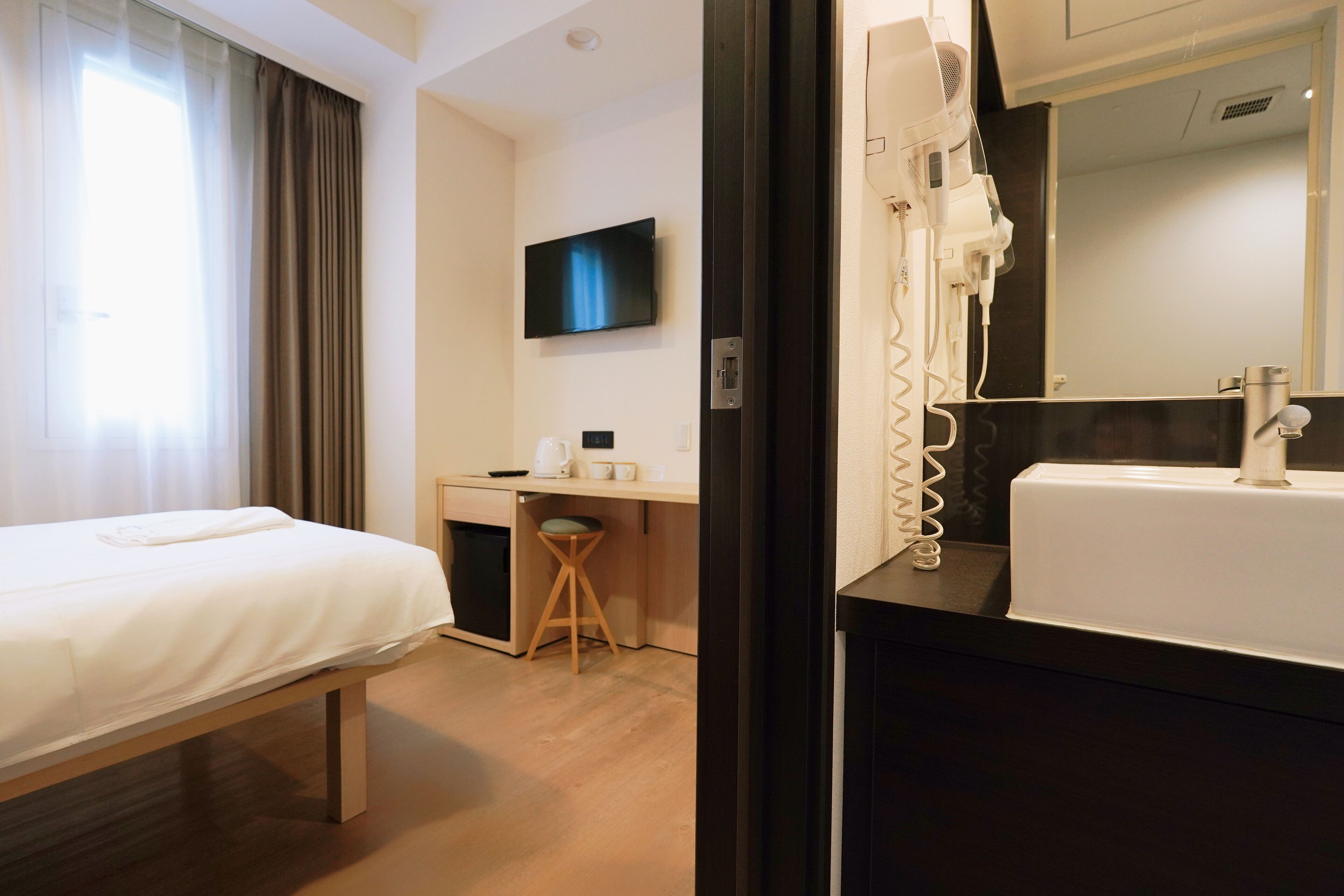 Hotelkamer met een bed, bureau, stoel, televisie, haardroger en wastafel.