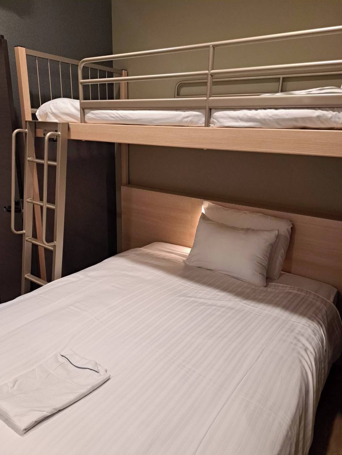 A bunk bed with a ladder, a single bed below, and a folded white towel on the lower bed.
