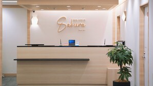 A reception desk with a sign reading "Sakura Hotel" and a digital screen. - Park Central Sakura Hotel (Osaka)