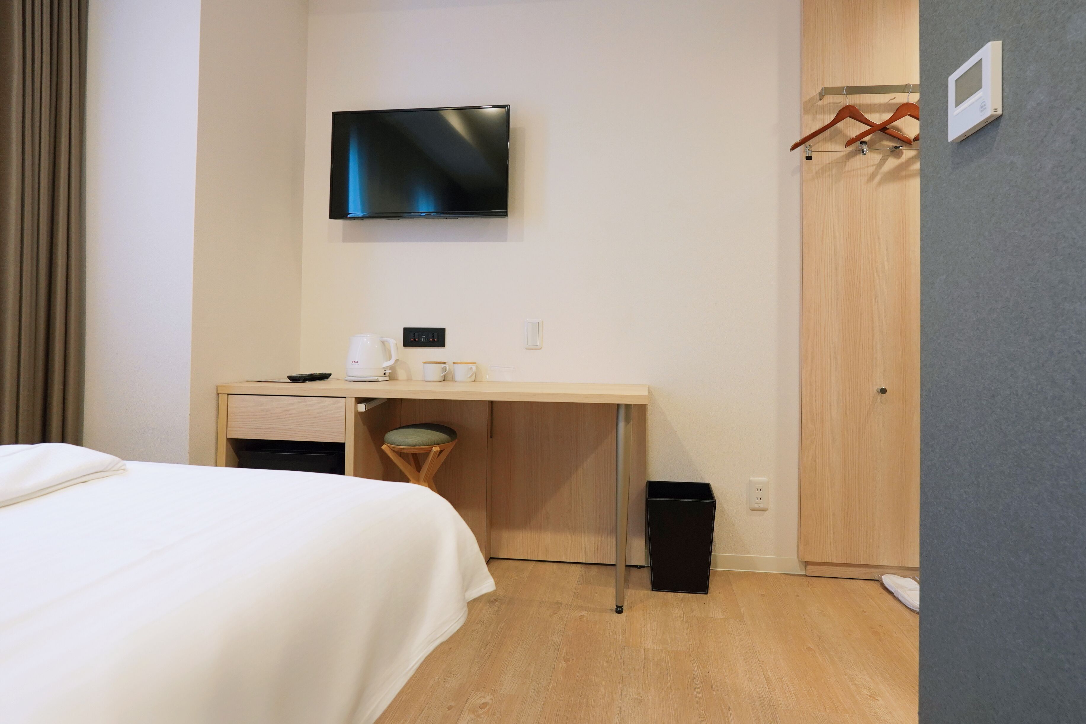 A hotel room with a bed, a desk with a flat-screen TV, a coffee maker, and a trash bin.