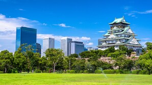 A traditional Japanese castle with multiple tiers and a green roof, surrounded by lush green trees and a clear blue sky. - Park Central Sakura Hotel (Osaka)