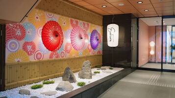 A lobby with a wall decorated with colorful umbrellas, a reception area with a hanging sign, and a rock garden with white pebbles and greenery.