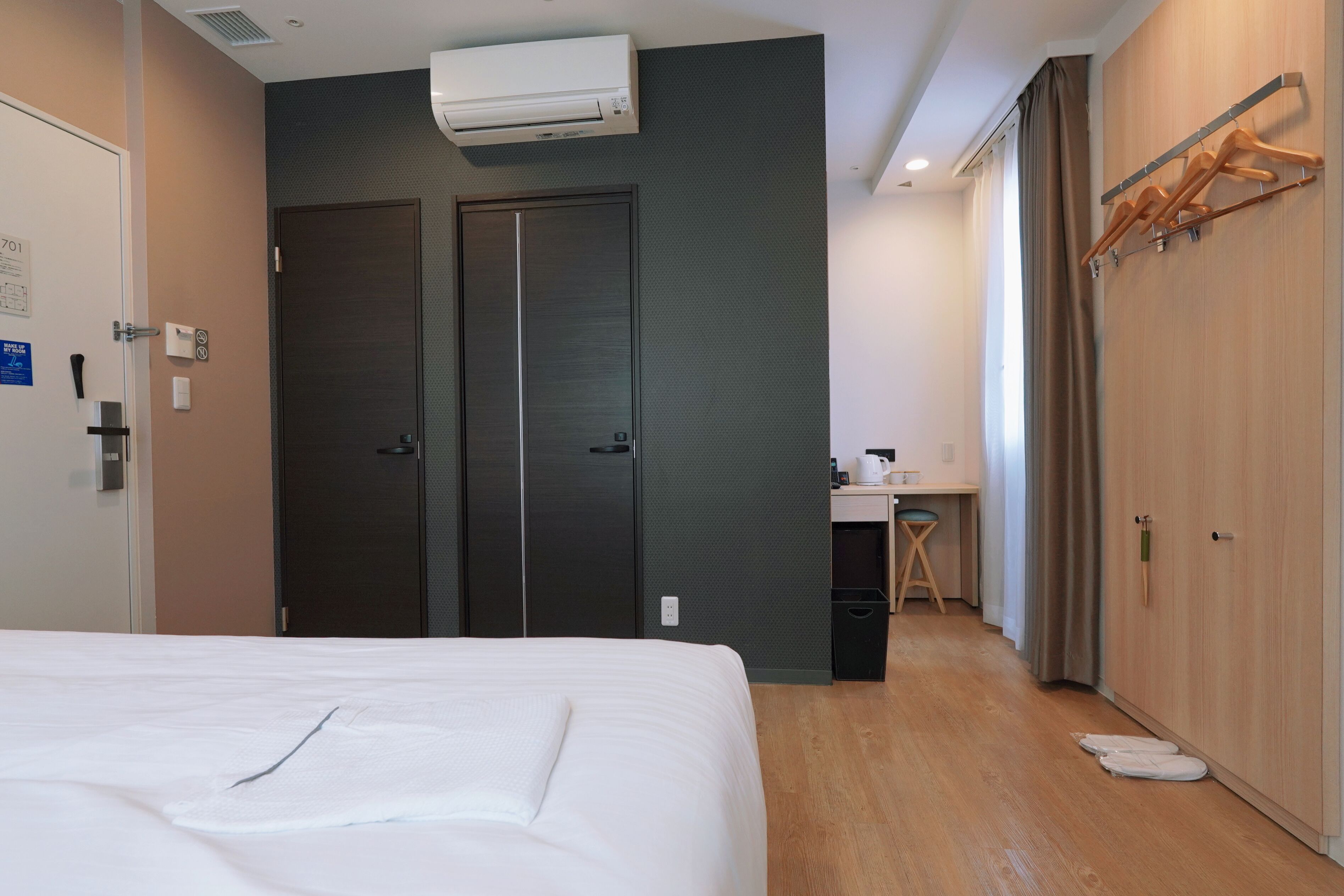 A hotel room with a bed, a desk, a wardrobe, and an air conditioning unit.