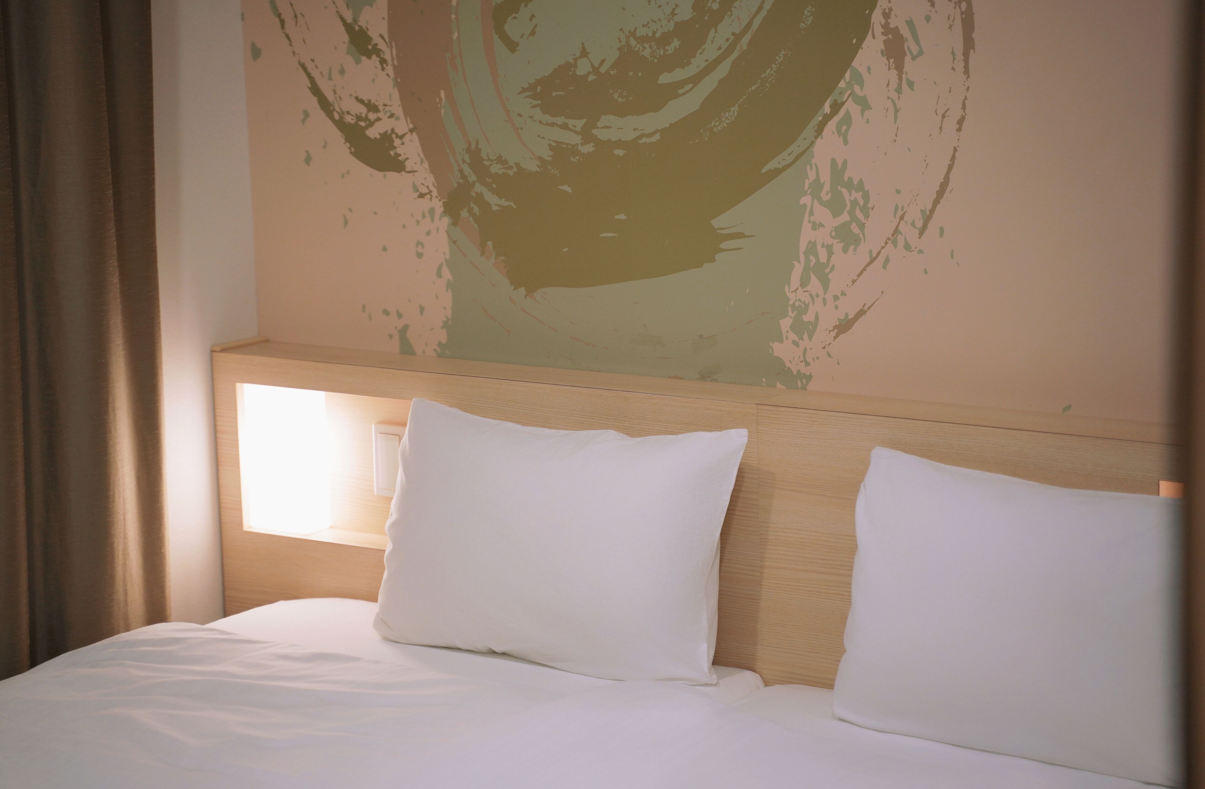 A hotel room with a wooden headboard, two white pillows, and a large abstract painting on the wall.