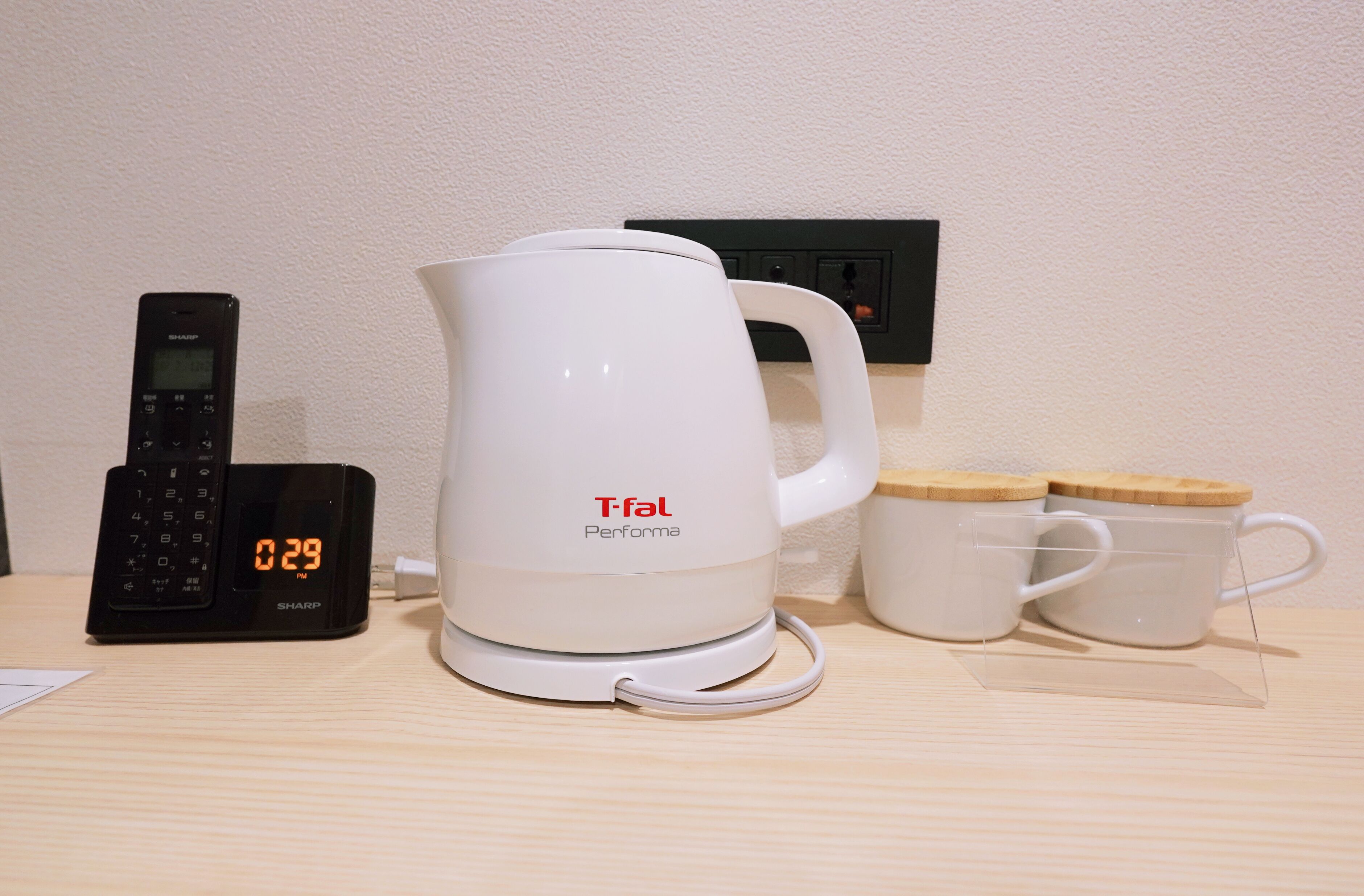 Una cafetera, un teléfono y dos tazas sobre una mesa de madera.