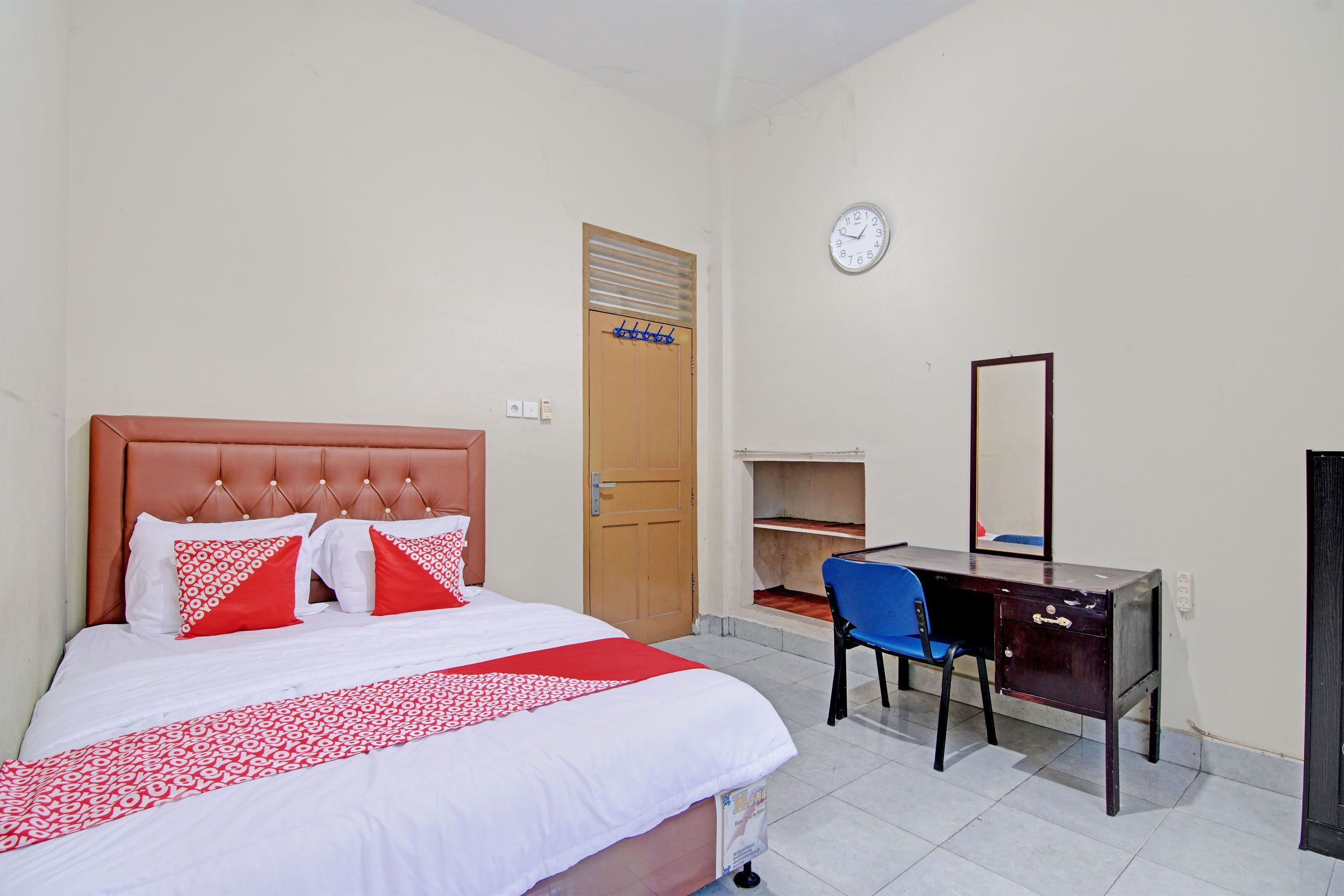A bedroom with a bed, a desk, a chair, a clock, and a door.