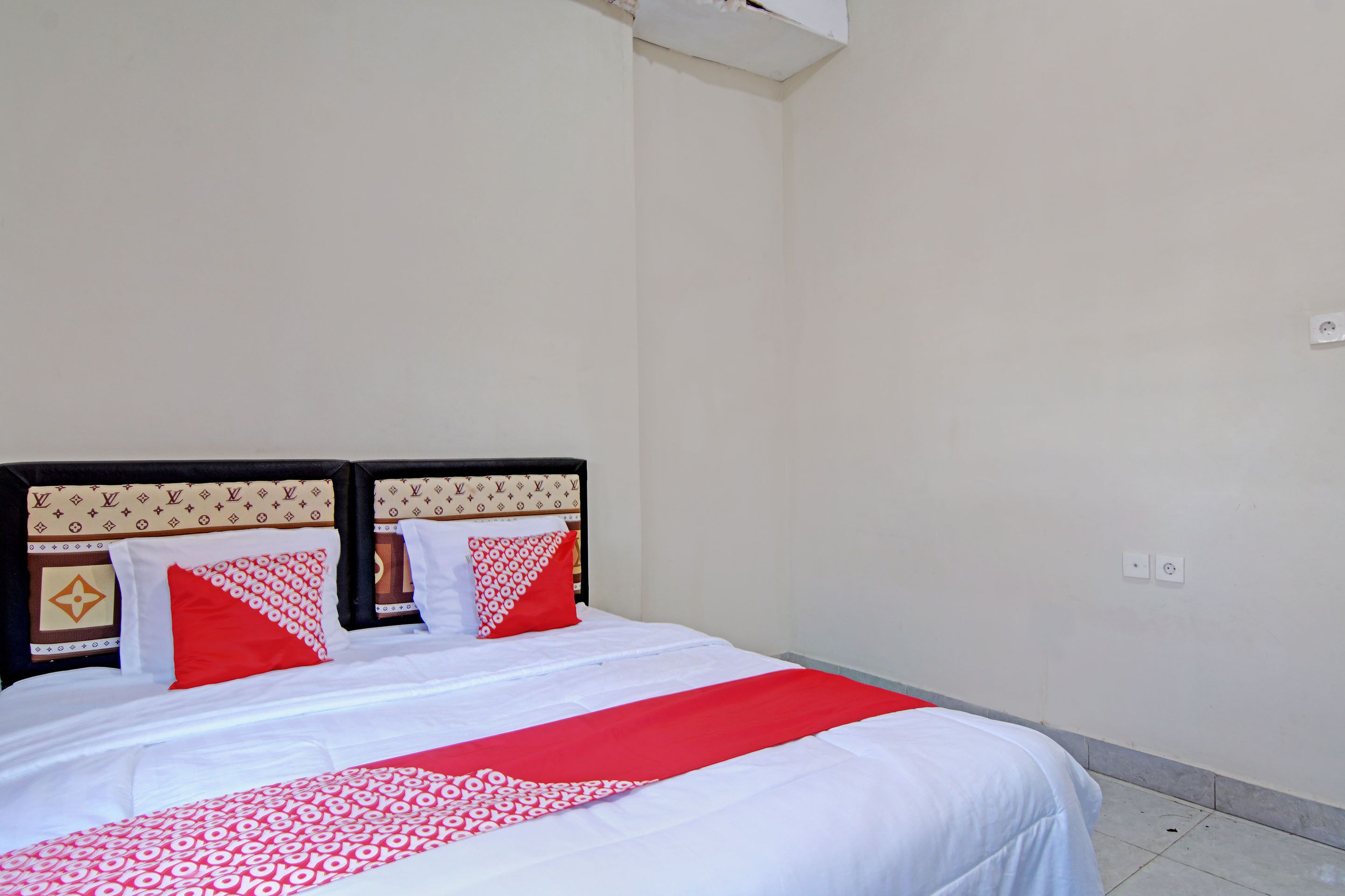 Una cama bien hecha con una colcha de cuadros rojos y blancos, un cabecero negro con diseño Louis Vuitton y dos almohadas rojas.