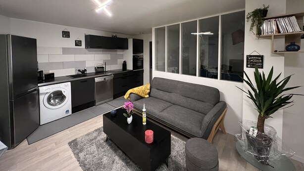 Ett modernt kök med inbyggd tvättmaskin och torktumlare, en grå soffa och ett soffbord med dekorativa föremål.