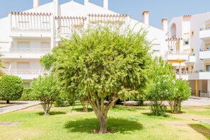 A building with multiple balconies and a well-maintained garden with a prominent tree.