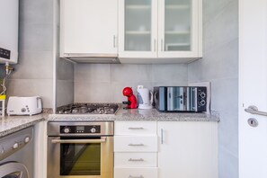 A compact kitchen with white cabinets, a built-in oven, a gas stove, a toaster, a kettle, and a coffee maker.