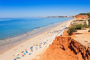 A beach with a clear sky, calm sea, and a rocky cliff.