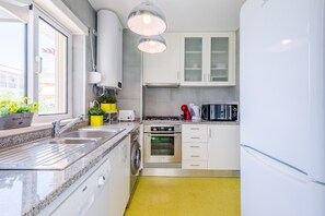 Et moderne køkken med vask, komfur, ovn og mikroovn. Et vindue giver naturligt lys, og der er en gul tæppe på gulvet.