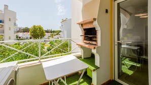 A balcony with a grill, a table, and a view of the neighborhood.