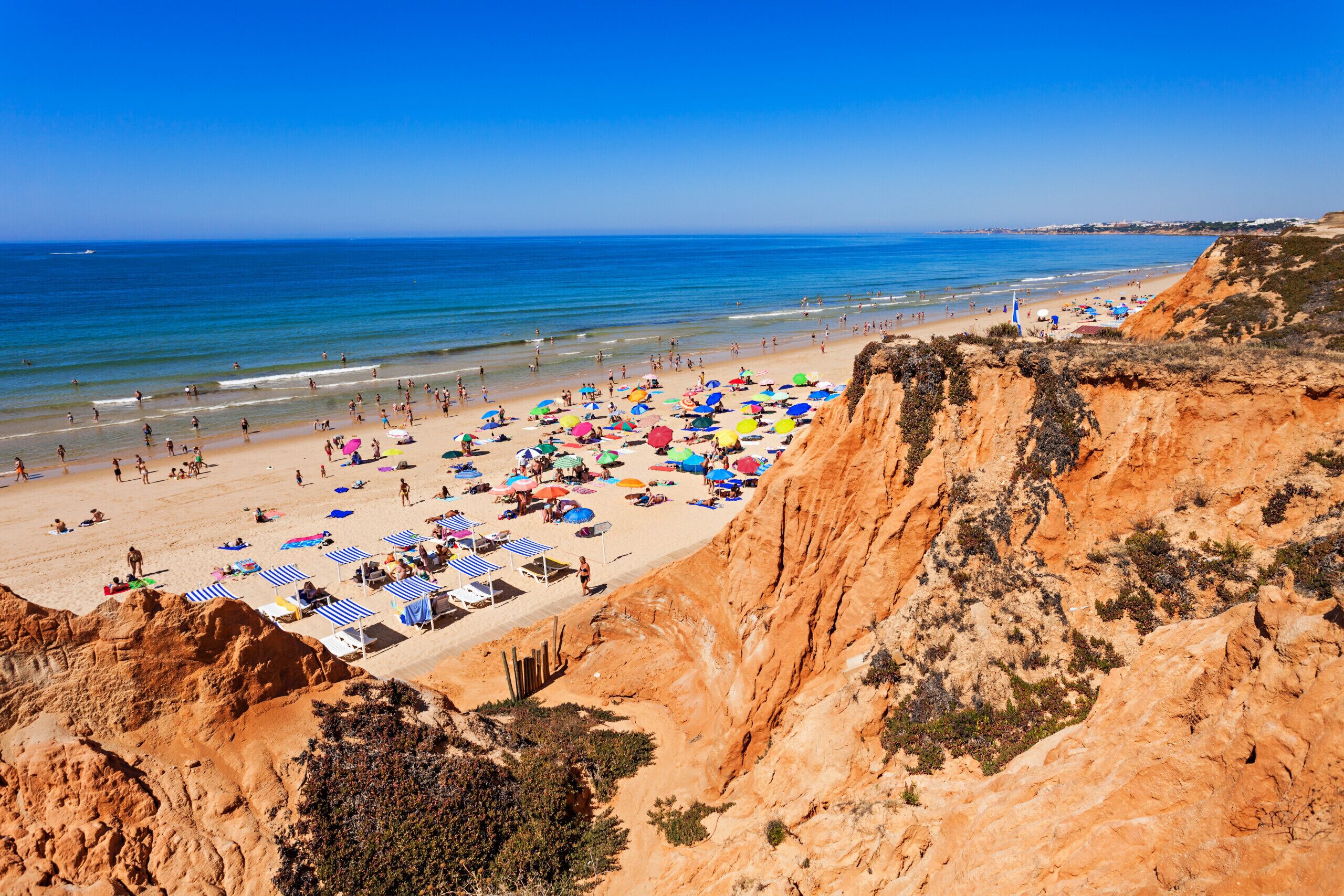 Une plage avec une falaise rocheuse, des parasols et des chaises longues.