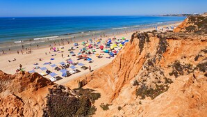 A beach with a rocky cliff, umbrellas, and sun loungers.