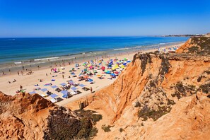 A beach with a rocky cliff, umbrellas, and sun loungers.