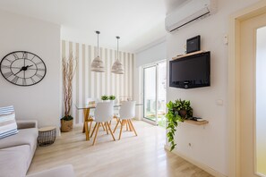 En moderne stue med en sofa, et spiseområde med et glasbord, og et fjernsyn ophængt på væggen.