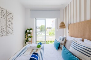 A bedroom with a bed, pillows, a bedside lamp, a window, and a balcony.