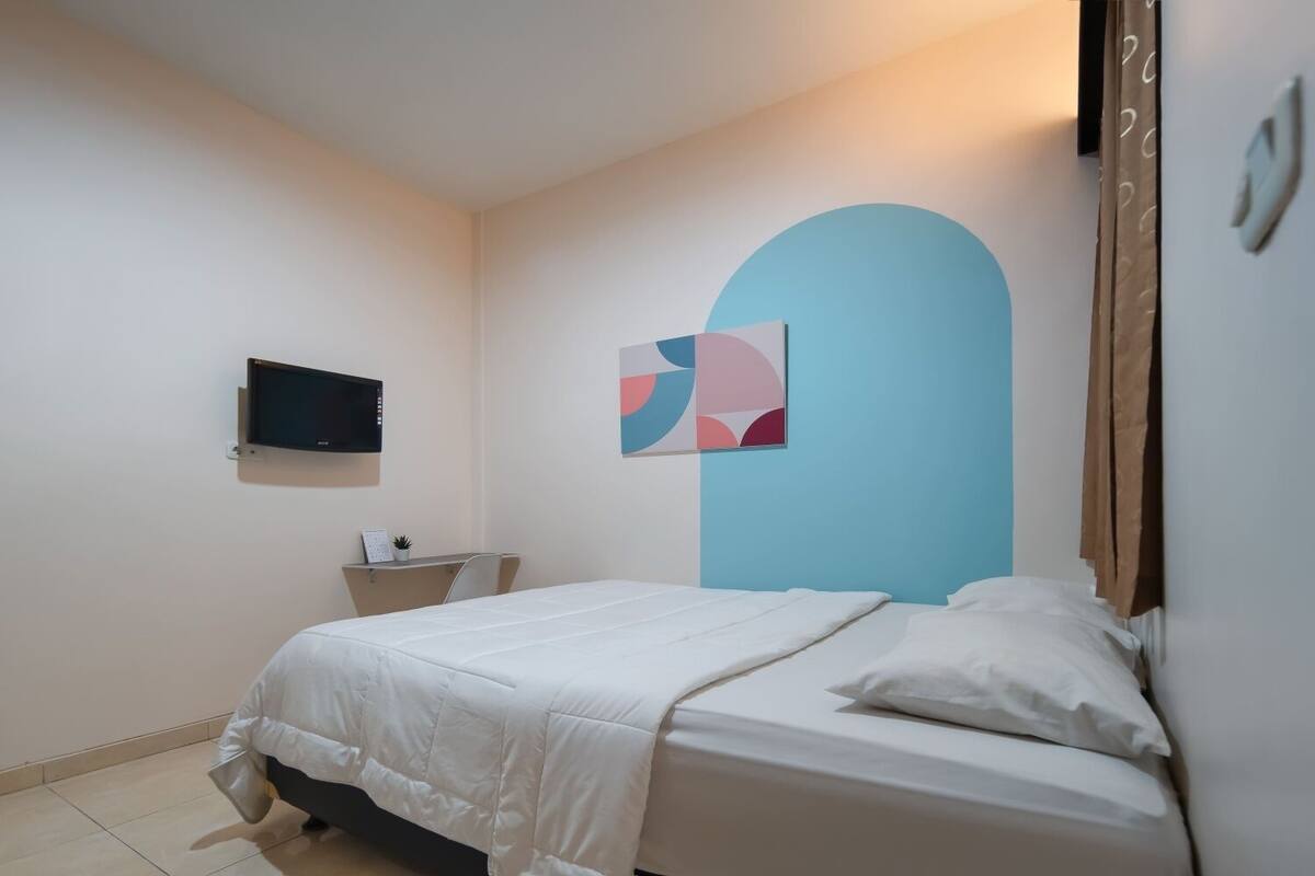 Um quarto com uma cama, uma escrivaninha, uma TV e uma obra de arte na parede.