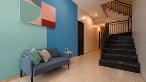 Un salon moderne avec un canapé bleu, une table basse et un tableau accroché au mur. Un escalier avec une rampe noire mène à l’étage supérieur.