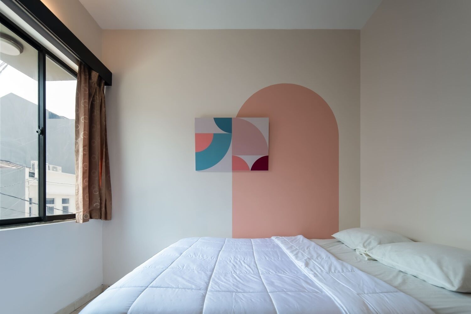 A hotel room with a bed, a window with curtains, and a wall-mounted abstract art piece.