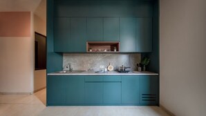 Une cuisine moderne avec des meubles de couleur turquoise, un plan de travail en marbre et une étagère intégrée au-dessus de l’évier.