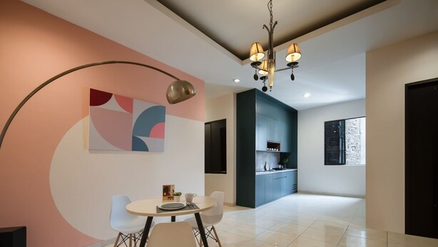 Un espace de salle à manger moderne avec une table ronde et des chaises, une cuisine en arrière-plan et des œuvres d’art abstraites accrochées au mur.