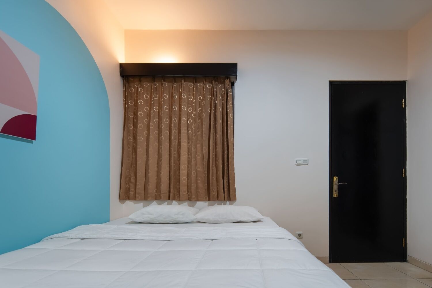 A bedroom with a bed, a door, and a wall with a partial circular design.
