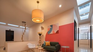 Un salon moderne avec un canapé, une table basse et un téléviseur. Il y a des luminaires au plafond et une grande fenêtre.