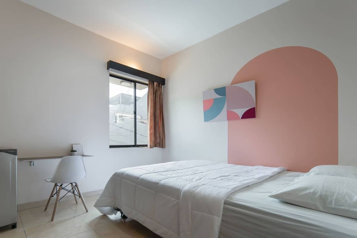 Quarto com uma cama, uma escrivaninha e uma janela.