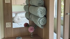 Ein Holzkabinett mit Spiegel, ein Ablagefach mit gerollten Handtüchern, eine Vase mit Blumen und ein Bett mit weißer Bettwäsche.