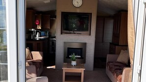 Ein Wohnzimmer mit Kamin, Fernseher und einer Küche im Hintergrund.