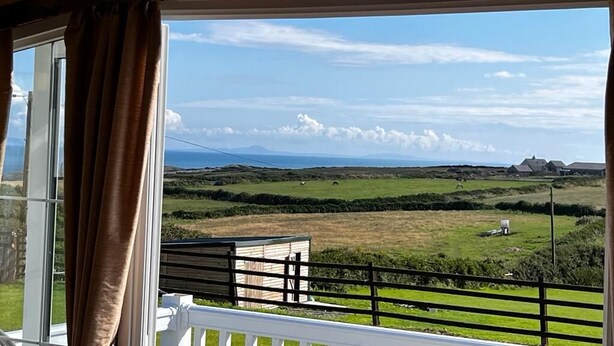Ein Zimmer mit großem Fenster, das einen Blick auf eine ländliche Landschaft mit Feldern, ein kleines Gebäude und ferne Hügel bietet.