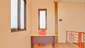 Une pièce avec un bureau, deux fenêtres et une rambarde rouge.