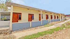 Un long bâtiment d’un seul étage, doté de nombreuses fenêtres et portes, d’un toit en béton et d’un chemin pavé menant à un escalier.
