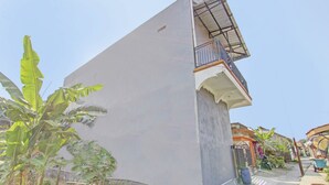 Un edificio residencial con un balcón, un pilar de hormigón y una palmera de plátano en primer plano.