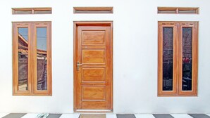 Una puerta de madera con felpudo, dos ventanas con marcos de madera y un suelo a cuadros.