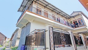 Un edificio residencial de dos pisos con balcón, entrada con reja y un espacio exterior cubierto.