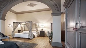 A bedroom with a four-poster bed, a bedside table with a lamp, a chair with a blanket, and a large mirror on the wall. - The style of Italian luxury close to the Duomo
 (Firenze)