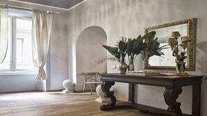 A room with a wooden floor, a dark console table with a mirror and lamps, a chair, and a large window with curtains. - The style of Italian luxury close to the Duomo
 (Firenze)