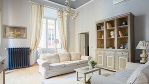 A living room with a beige sofa, a glass coffee table, a cabinet with glass doors, and a chandelier. - The style of Italian luxury close to the Duomo
 (Firenze)