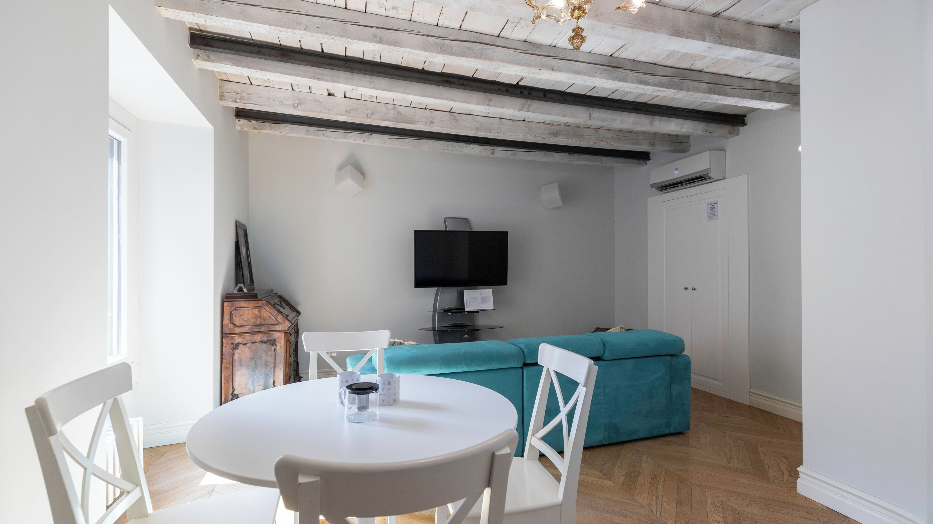 A dining area with a round table and chairs, a blue sofa, and a flat-screen TV mounted on the wall.