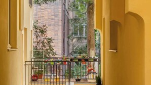 A corridor with a tiled floor, a metal gate, and a view of a tree and buildings outside. - TurnKey | Two level Charles Square Apartment I (Praha 2)