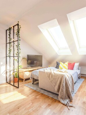 A bedroom with a bed, a TV, a plant, and a skylight.