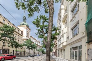 A street with buildings, a tram, and a tree. - TurnKey | Charles Square Apartment – with Balcony (Praha 2)