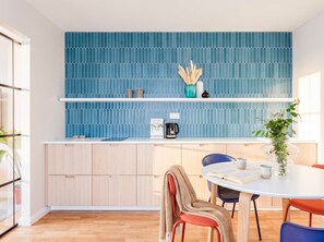 A modern kitchen with a blue patterned backsplash, wooden cabinets, and a dining area with a round table and chairs. - TurnKey | Charles Square Apartment – with Balcony (Praha 2)