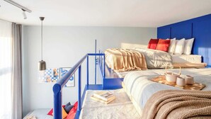 A modern bedroom with a bunk bed, a blue railing, a hanging light fixture, and a view of the sea. - TurnKey | Charles Square Studio – with Terrace (Praha 2)