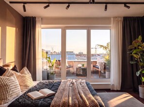 Un dormitorio moderno con una cama grande, vistas de la ciudad a través de ventanales del piso al techo y un balcón con mobiliario exterior.
