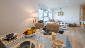 Un coin repas avec une table dressée pour quatre personnes, un saladier de fruits et une horloge au mur.