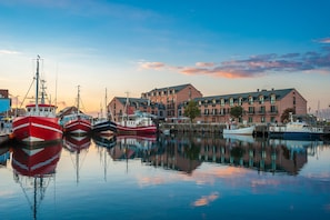 A marina with several boats docked, a large building with multiple windows and balconies, and a calm water surface reflecting the boats and building. - CBlue "Küstenzauber" with Balcony (Heiligenhafen)